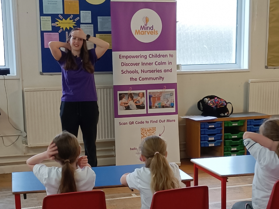 Karen leading a Mind Marvels session with children with hands on their heads.