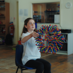 A child with the breathing sphere in Mind Marvels session, sat on a chair.