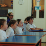 Children listening at their desks and smiling at a Mind Marvels session