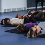Adults and children lie on mats through a guided meditation at a Mind Marvels session