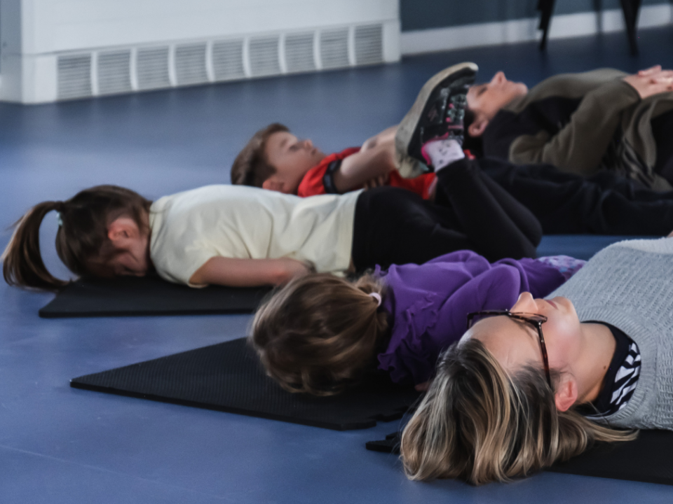 Adults and children lie on mats through a guided meditation at a Mind Marvels session