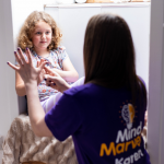 Karen showing a child a breathing technique called finger breathing using her hand as girl sits on window seat watching.