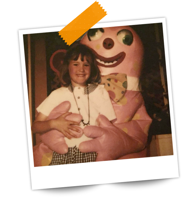 Karen as a child standing in front of a person in a Mr Blobby costume, smiling.